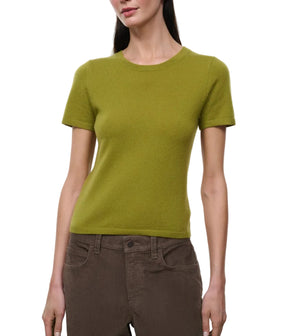A woman wearing the Staud Easy Cashmere Tee in green, featuring short sleeves and a crew neckline, paired with brown pants stands against a plain white background.