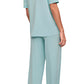 A person stands barefoot, facing away, wearing the Eberjey Gisele Short Sleeve Long Pant PJ Set in light blue; it includes a classic fit top with short sleeves and low-rise straight leg pants featuring an elastic waistband.