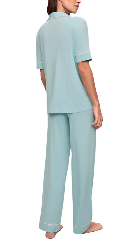 A person stands barefoot, facing away, wearing the Eberjey Gisele Short Sleeve Long Pant PJ Set in light blue; it includes a classic fit top with short sleeves and low-rise straight leg pants featuring an elastic waistband.