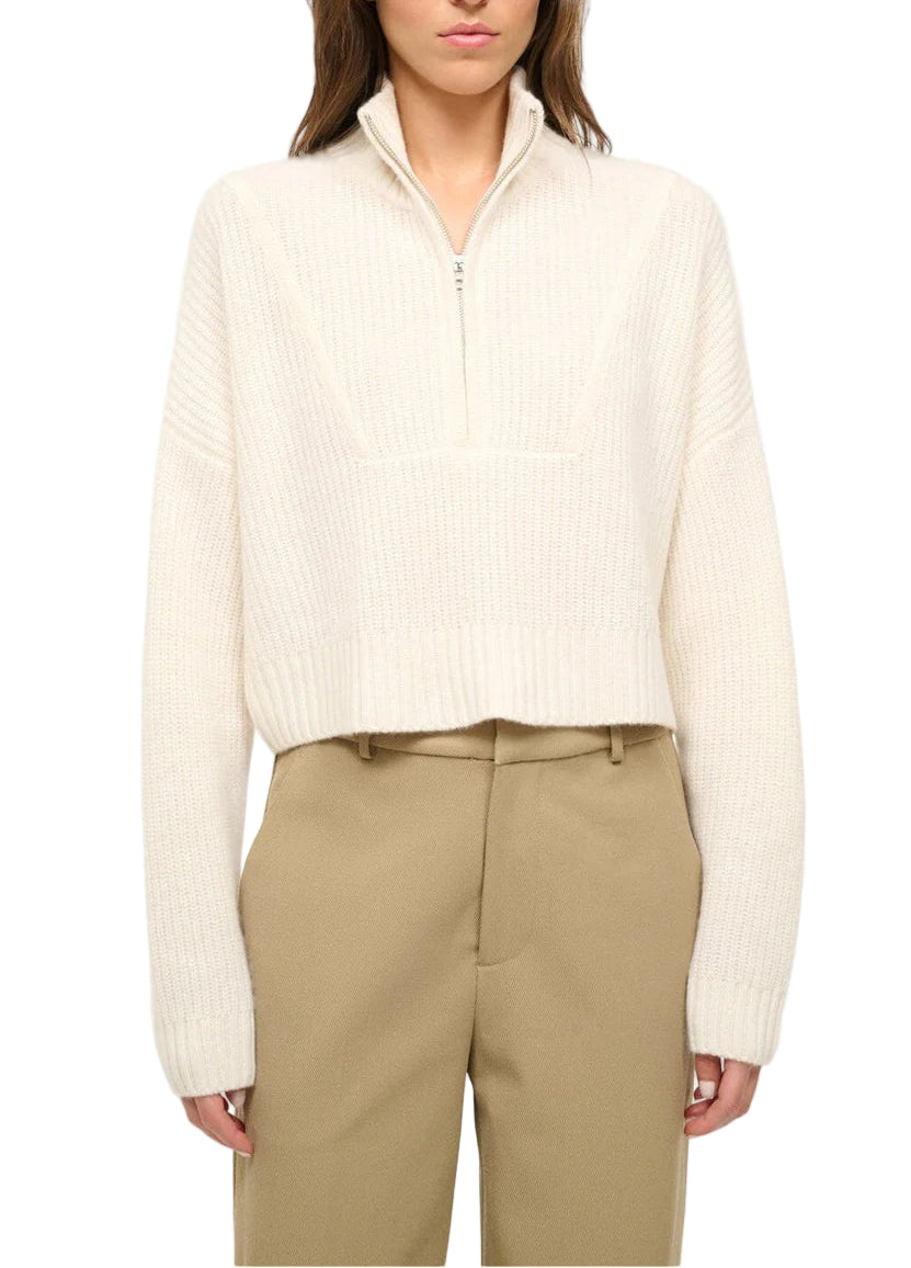 A person wearing a cream Cropped Hampton Cashmere Sweater by Staud with beige high-waisted trousers, waist up against a white background.