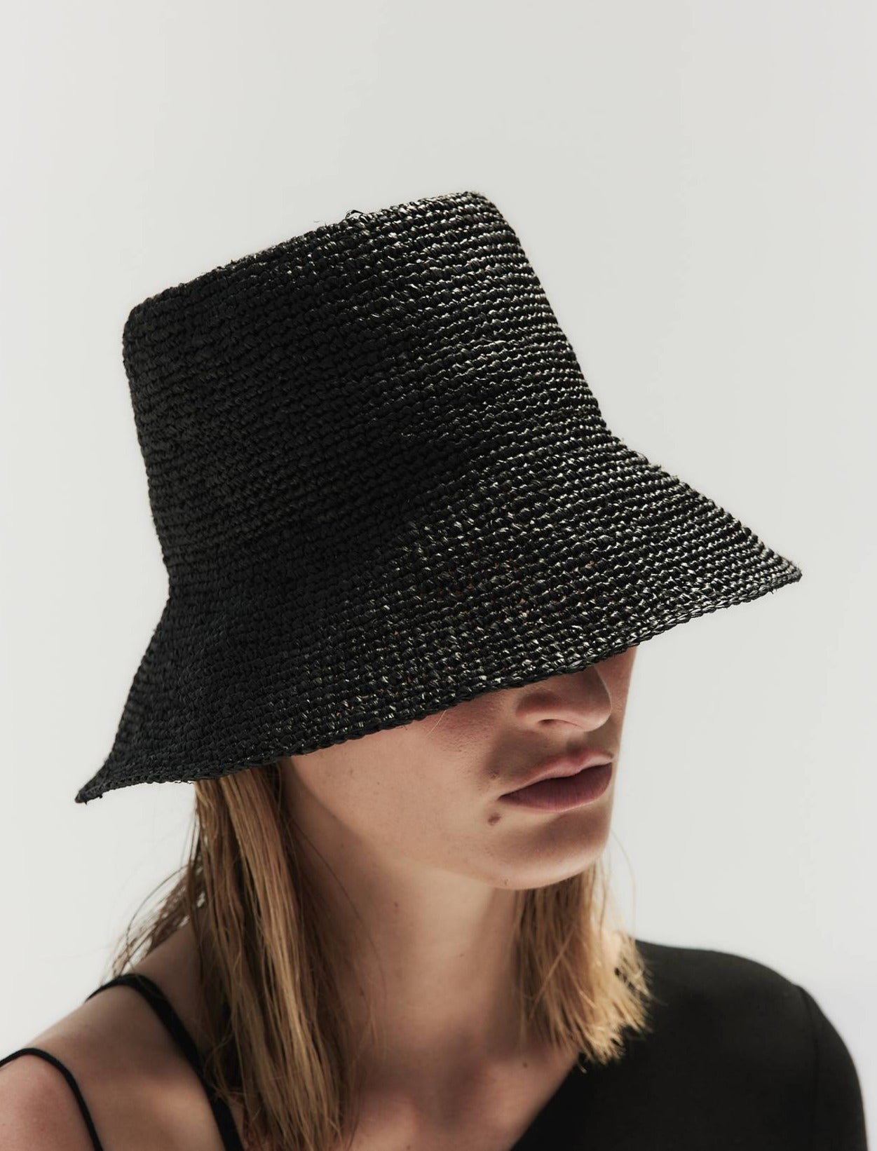 A person wearing a large black Janessa Leone Felix hat that covers their eyes, against a plain white background.