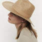 Profile of a woman wearing a Janessa Leone Simone Hat with UPF 45+ protection and a light beige jacket against a white background.