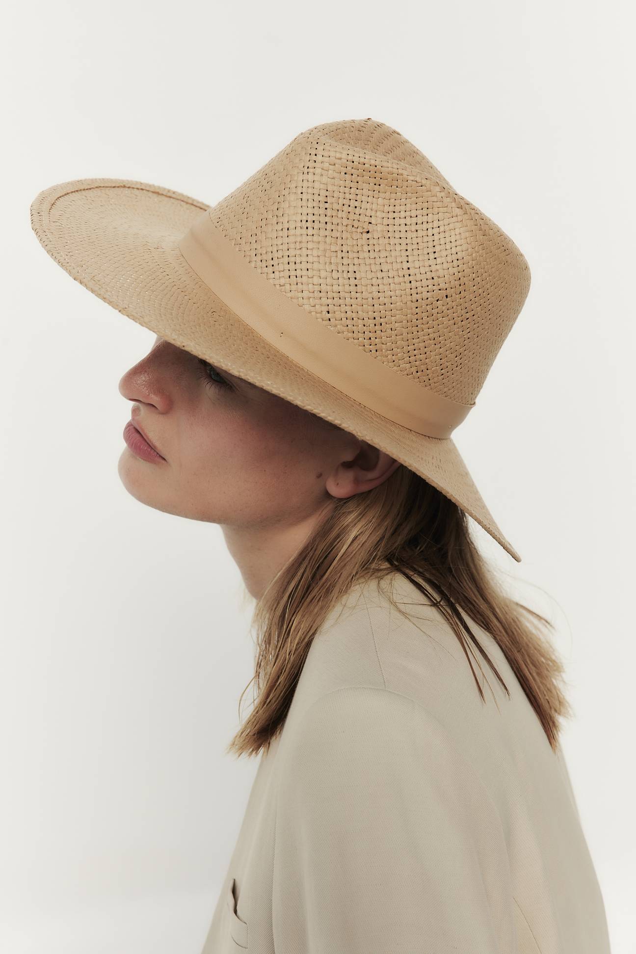 Profile of a woman wearing a Janessa Leone Simone Hat with UPF 45+ protection and a light beige jacket against a white background.