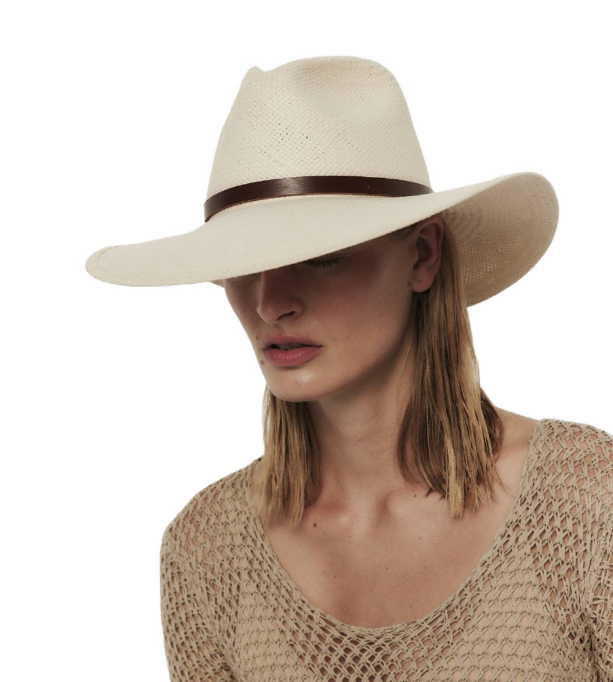 Woman with her head tilted down, wearing a wide-brimmed white UPF 35+ Janessa Leone Judith Hat and a beige textured top, isolated on a white background.