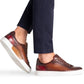 Person wearing dark brown Magnanni Amadeo Sneaker leather sneakers with white soles and navy blue pants, embodying contemporary cupsole fashion.