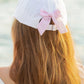 A person with long brown hair wears the Bits & Bows Birthday Girl Bow Baseball Hat, featuring a white design and a pink and white seersucker bow on the back.