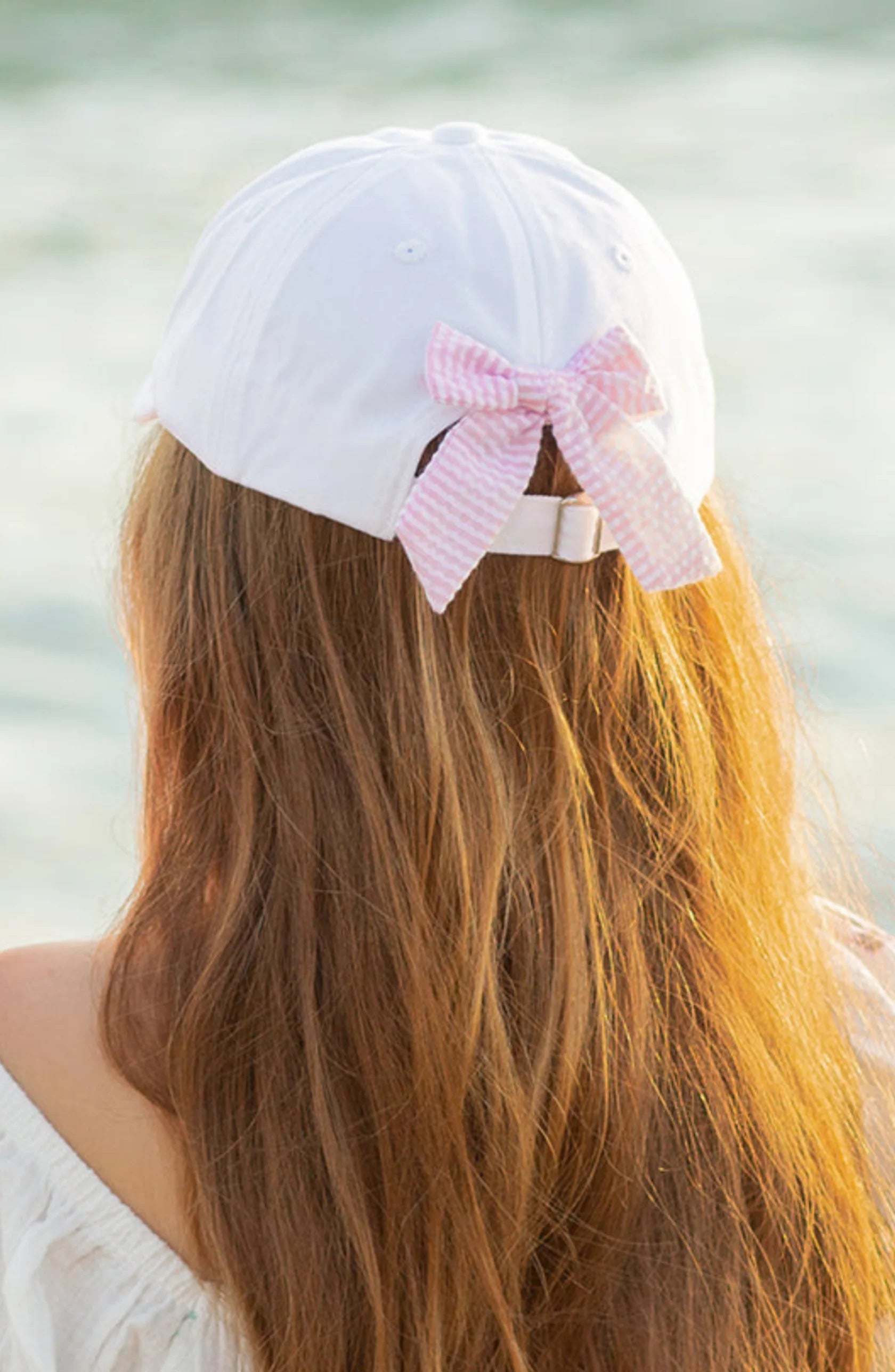 A person with long brown hair wears the Bits & Bows Birthday Girl Bow Baseball Hat, featuring a white design and a pink and white seersucker bow on the back.