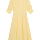 The Simkhai Jazz Pintuck Midi Dress, in light yellow cotton poplin, features a collar, long sleeves with button details, and an A-line silhouette, shown laid flat on a white background.