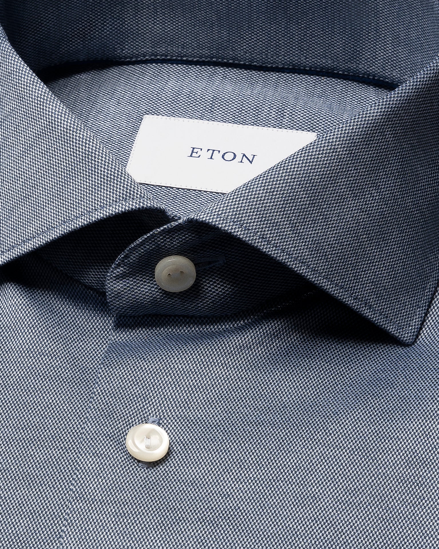 Close-up of a blue Slim Wide Spread Filo di Scozia Knit Shirt by Eton, featuring white buttons and a visible Eton label inside the collar.