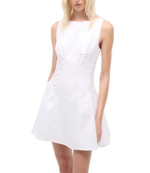 A woman models the Staud Gwen Mini Dress—a sleeveless, white poplin A-line style with a fitted waist and structured pleats on its flared skirt—against a plain background.