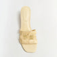 The Simkhai Monogram Raffia Flat Slide by Simkhai features a beige woven design, open toe, square sole, and two wide cut-out straps—sleek flats perfect for any casual look, shown on a plain white background.