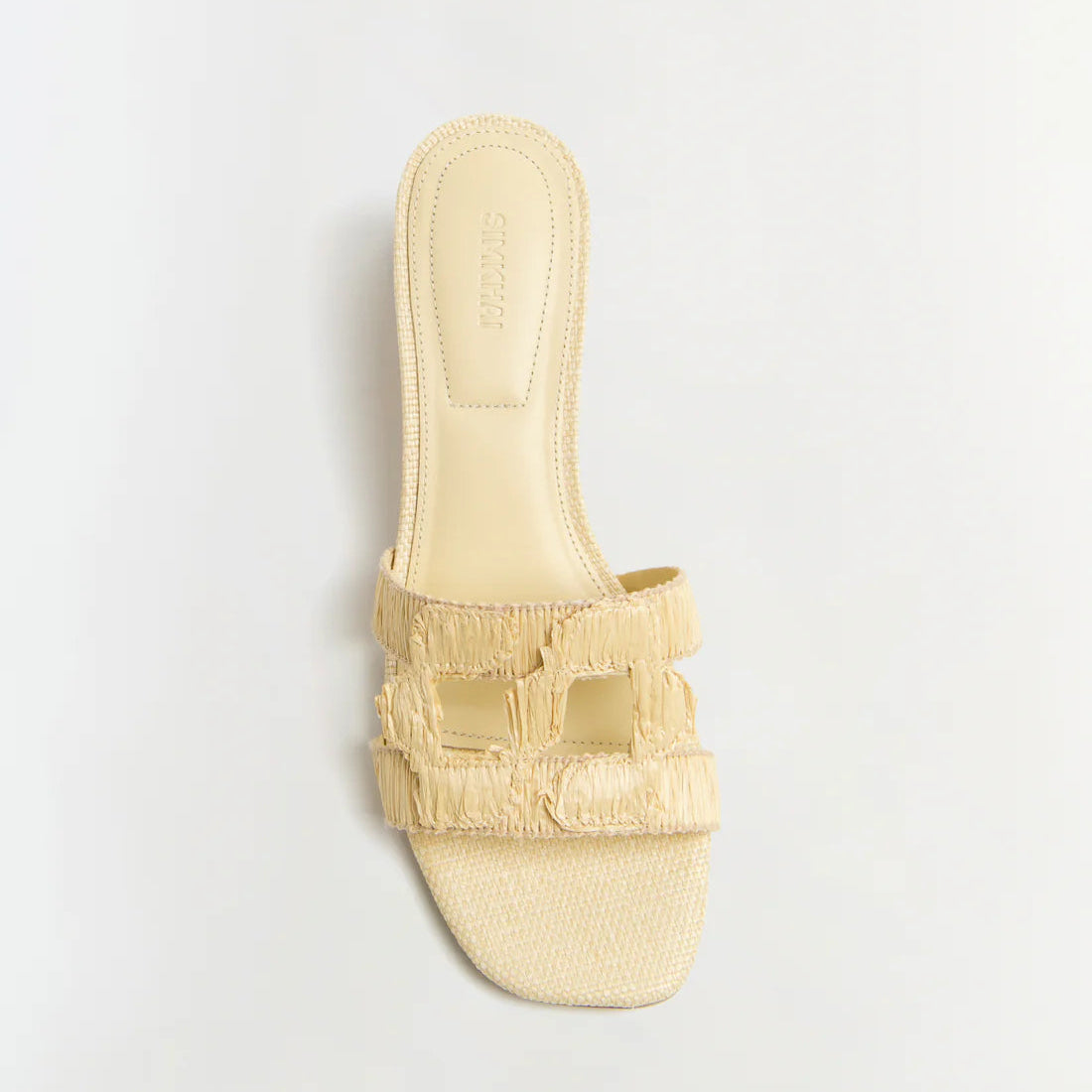 The Simkhai Monogram Raffia Flat Slide by Simkhai features a beige woven design, open toe, square sole, and two wide cut-out straps—sleek flats perfect for any casual look, shown on a plain white background.