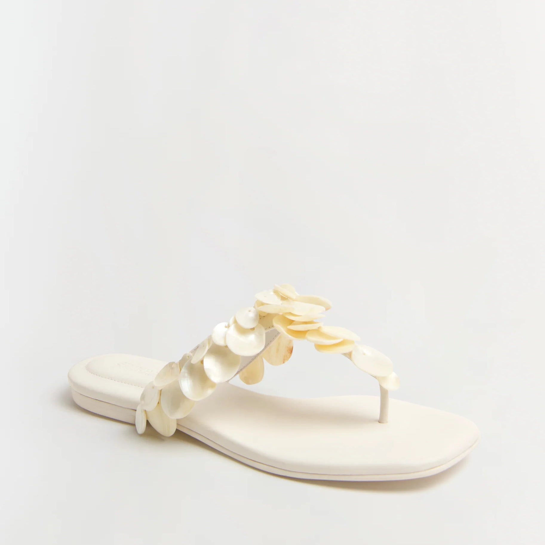 The Simkhai Elin Natural Shell Beaded Thong Sandal is a white flat sandal featuring a thong silhouette and layered shell bead embellishments for an elegant look.