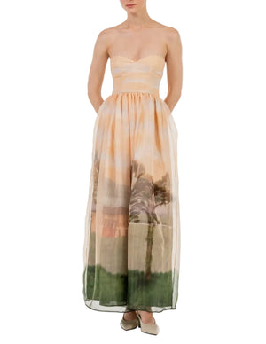 Confident woman wearing the Tonia Dress by Agua By Agua Bendita, a strapless occasion dress featuring a striking landscape print and handy pockets.