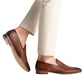A person wears light beige pants with elegant Herrera Woven Loafers by Magnanni, feet slightly elevated, highlighting the perfect blend of comfort and classic style from the Línea Flex collection.