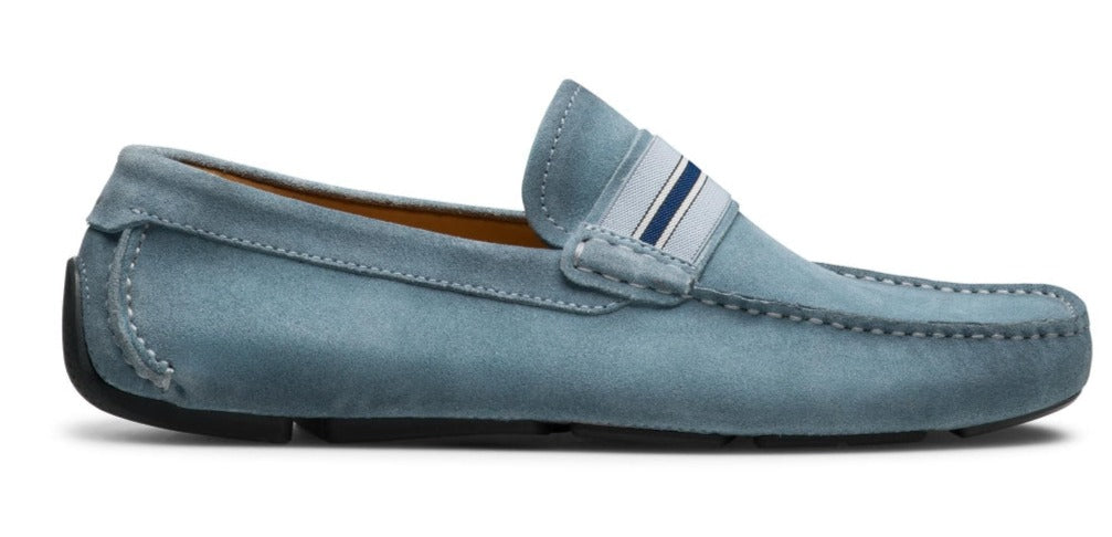 A side view of a modern driving shoe with a supple suede upper and a rubber sole. The Magnanni Loira Loafer by Magnanni features hand-stitched moccasin detailing and a small section of striped fabric on the tongue.