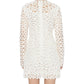 A person is shown from the back wearing the Simkhai McCall Mini Dress, a long-sleeved white lace shift with delicate crochet embroidery, against a plain white background.