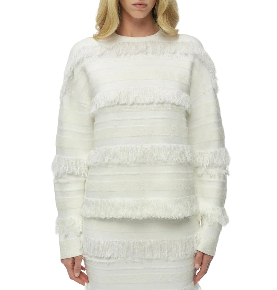 A woman models the Simkhai Carrick Crewneck Sweater, a white knit with long sleeves, horizontal stripes, and fringe accents, standing against a plain background.