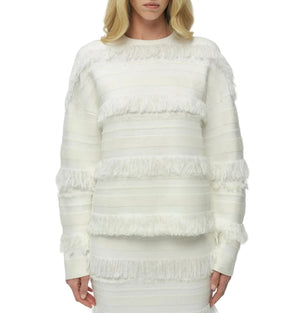 A woman models the Simkhai Carrick Crewneck Sweater, a white knit with long sleeves, horizontal stripes, and fringe accents, standing against a plain background.