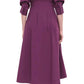 A person wearing the Simkhai Signature Jazz Dress in purple, with sleeves rolled up, is seen from the back, standing gracefully on beige heels. The tailored bodice and elegant pintuck detailing of the dress contribute a touch of sophistication to the ensemble.