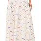A woman stands with her back to the camera wearing the Staud Procida Linen Skirt, a high-waisted, ankle-length cream maxi skirt featuring a colorful sardines print.