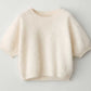 The Juniper Brushed Cashmere Sweater by Lisa Yang is a short-sleeved, cream cropped sweater with a round neckline, shown against a light gray background.