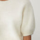 Close-up of a person wearing the Lisa Yang Juniper Brushed Cashmere Sweater, a short-sleeved, white crewneck, set against a plain background.