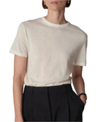 A person wears a relaxed silhouette featuring a white CO Cashmere Tee tucked into black pants, with hands in pockets. They accessorize with a watch and hoop earrings.