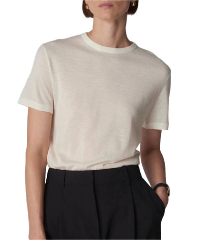 A person wears a relaxed silhouette featuring a white CO Cashmere Tee tucked into black pants, with hands in pockets. They accessorize with a watch and hoop earrings.