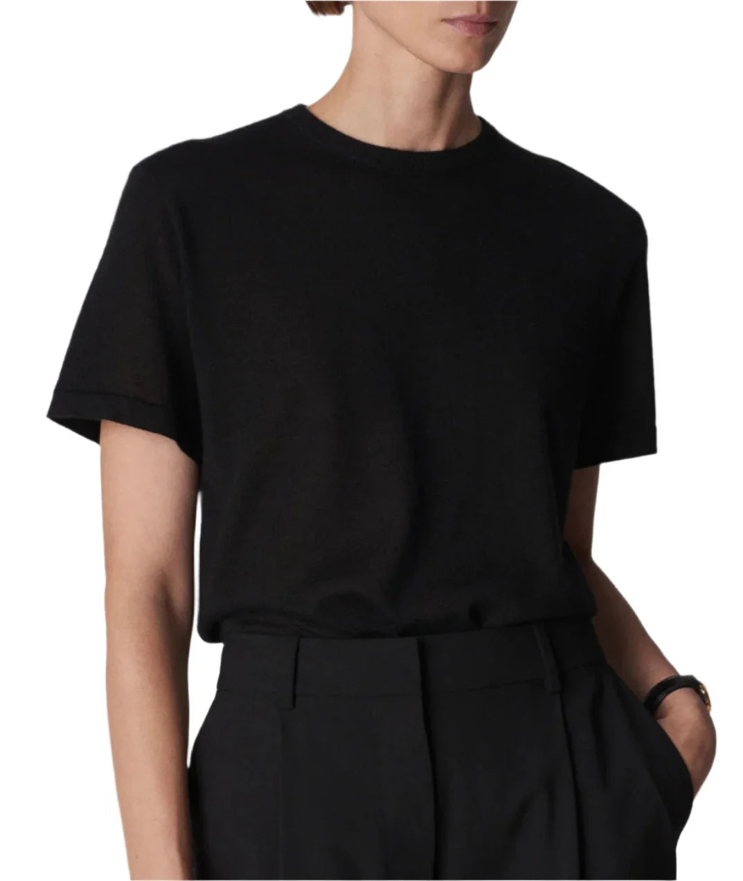 Person wearing a CO Cashmere Tee in black, featuring short sleeves and a lightweight feel, tucked into high-waisted black pants. Arms are relaxed at their sides and the face is partially out of frame.