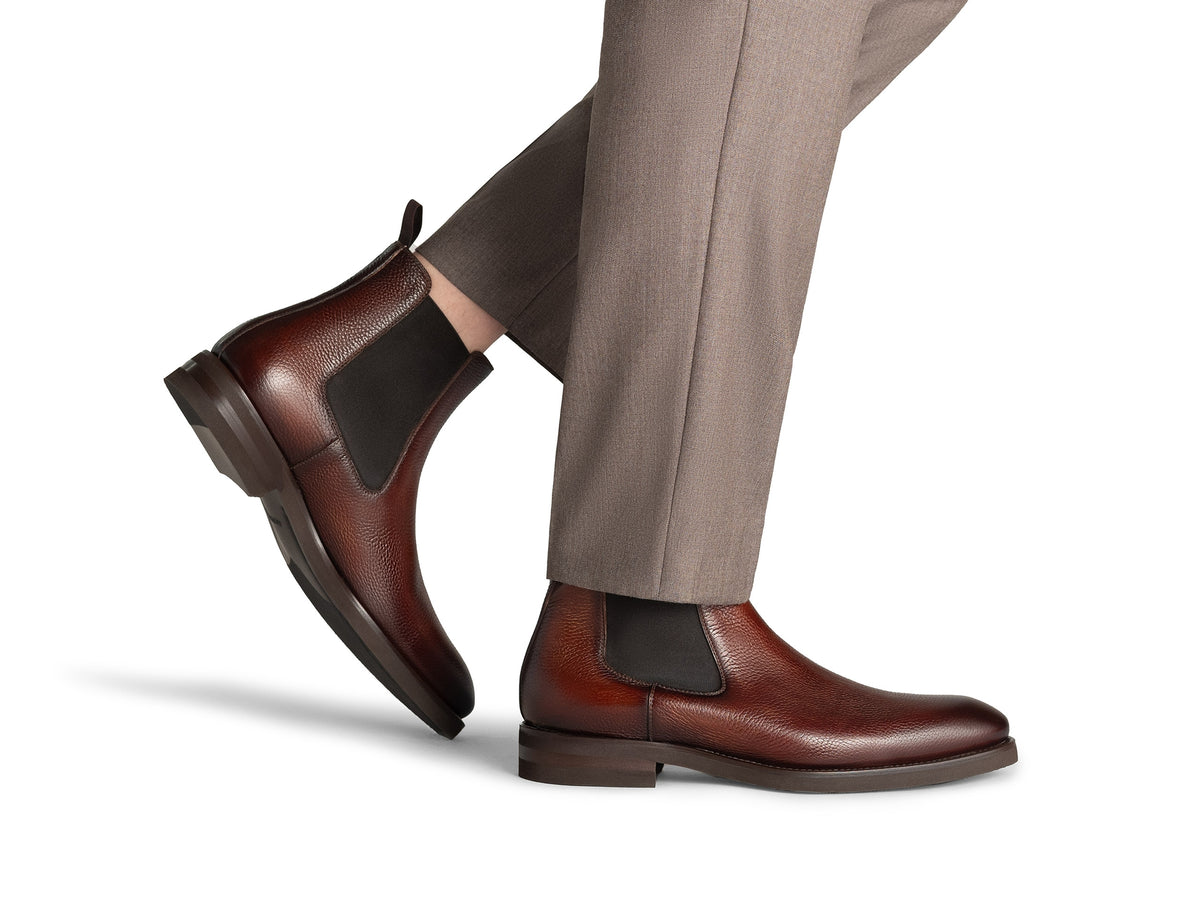 A person wearing Magnanni Lonny Chelsea boots with dark elastic side panels and gray trousers.