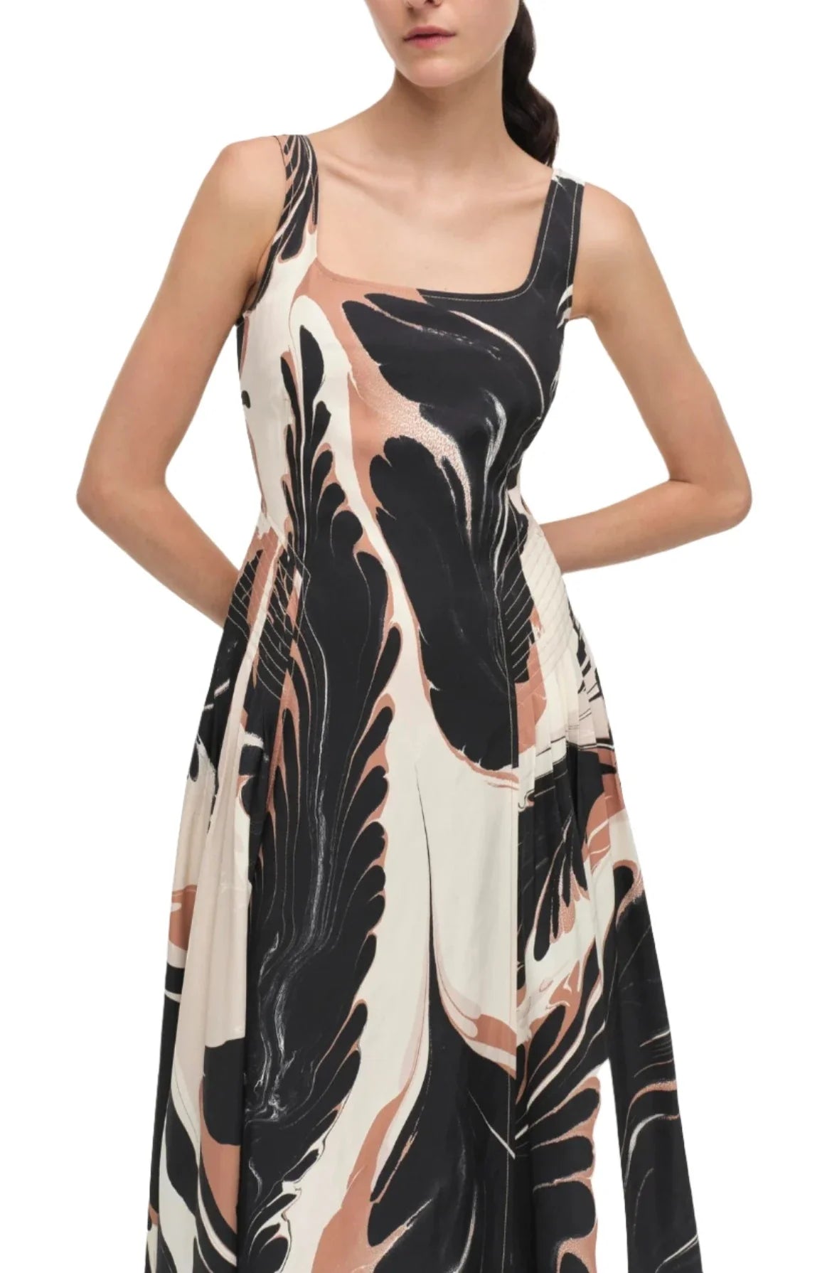 A person is wearing the Simkhai Paola Midi Dress, featuring a sleeveless, square-neck design with a black, white, and peach abstract print. The flattering silhouette is complemented by the person's hands in the dress's pockets.