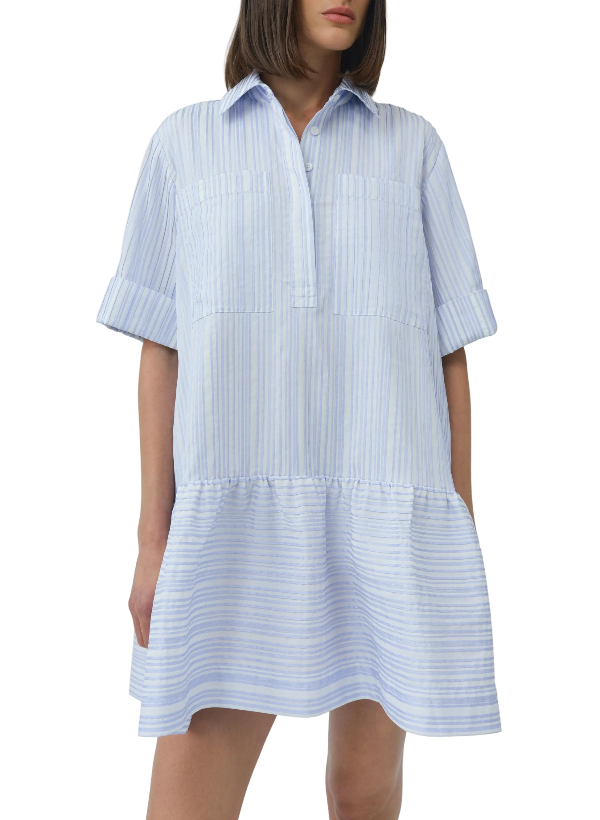 A woman wears the Simkhai Cris Short Sleeve Shirt Dress featuring blue stripes, a collared neckline, loose fit, and ruffled hem.