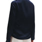 A person in a dark TWP Phoebe Top by TWP and light-colored pants creates an elongated silhouette while facing away from the camera against a plain background.