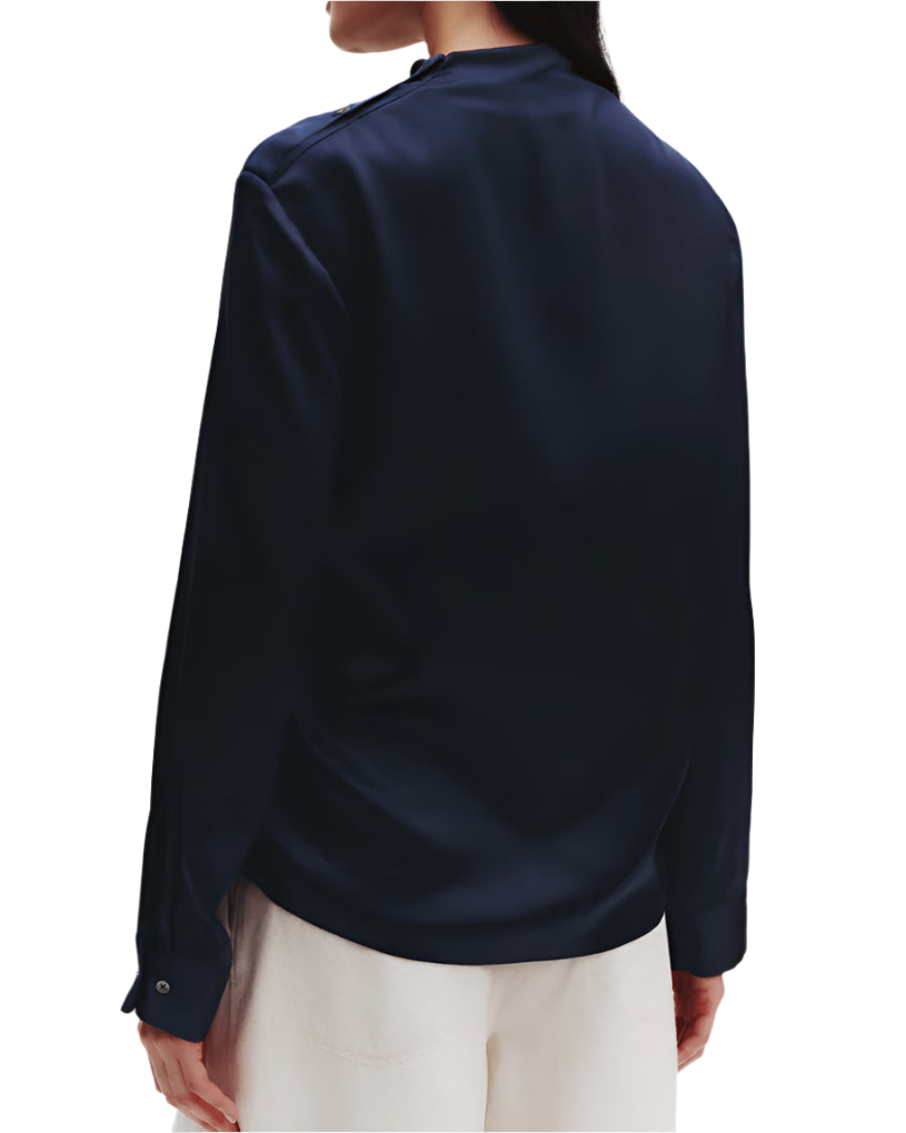 A person in a dark TWP Phoebe Top by TWP and light-colored pants creates an elongated silhouette while facing away from the camera against a plain background.