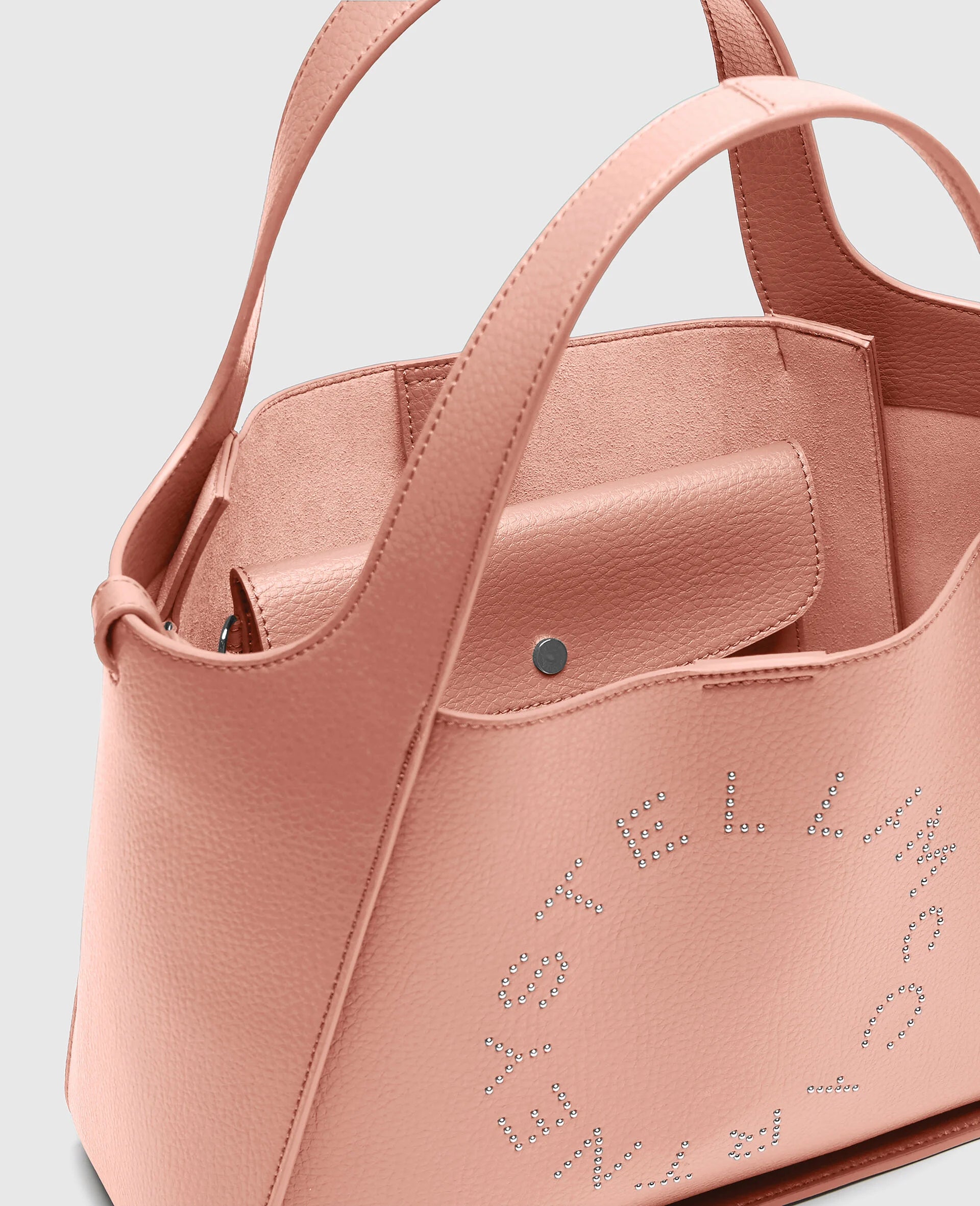 Close-up of the Stella McCartney Logo Crossbody Tote Bag in pink vegan leather, featuring a snap-button pouch inside and perforated logo branding on the exterior.