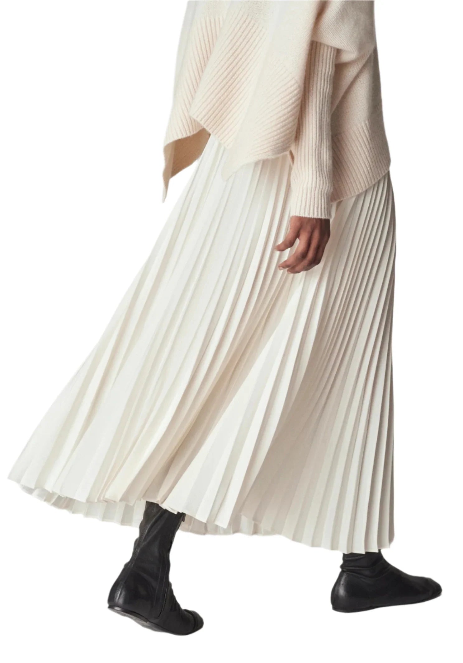 A person wearing a cream-colored top and a CO Pleated Elastic Waist Skirt from CO, paired with black ankle boots, walks.