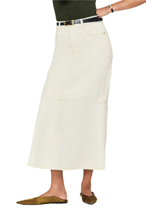 A person wearing The Flounce Denim Skirt by Frame, a cream-colored maxi with front pockets, styled with a black belt and brown flat shoes. Upper body is not visible.