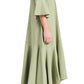 A person is standing sideways wearing the Dorothee Schumacher Summer Cruise Maxi Dress, a light green linen blend dress with flared sleeves and hem, paired with beige sandals.