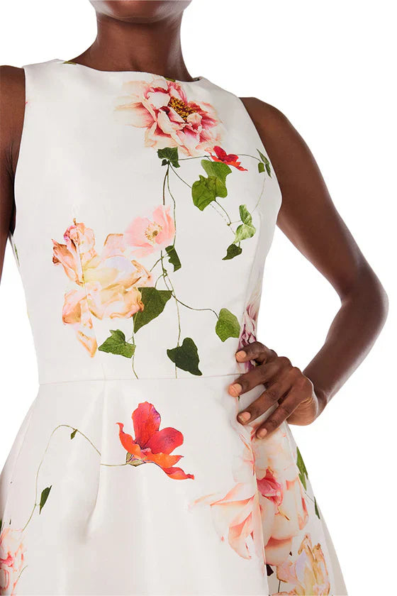 A person wearing a Monique Lhuillier Jewel Neck Slvls Fit and Flare Dress showcases a stunning floral pattern of pink and red flowers on a fit & flare midi-length dress by Monique Lhuillier.