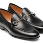 The Magnanni Stella Loafer is a pair of black leather slip-on shoes, showcasing traditional apron toe styling and adorned with metal horsebit detailing on top.