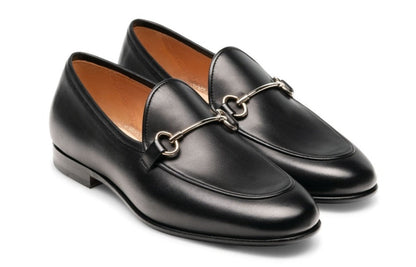 The Magnanni Stella Loafer is a pair of black leather slip-on shoes, showcasing traditional apron toe styling and adorned with metal horsebit detailing on top.