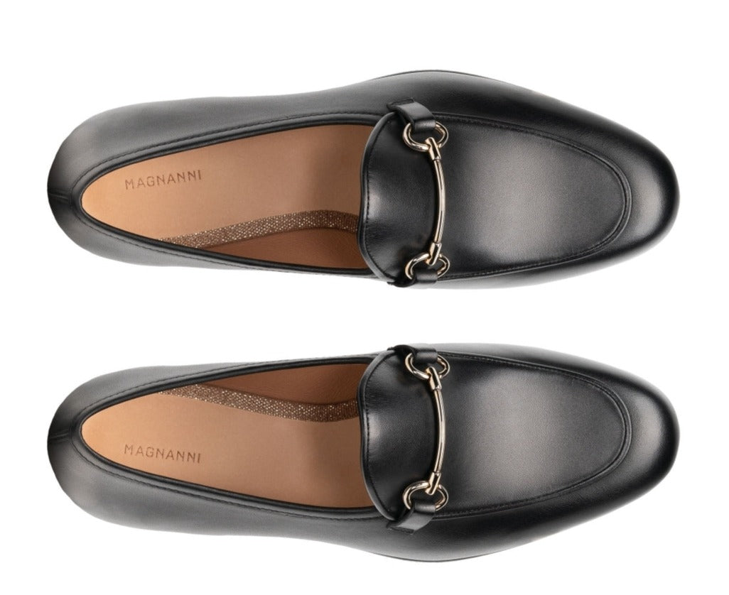 Magnanni Stella Loafers by Magnanni are stylish black leather apron toe loafers featuring elegant gold buckles, highlighted from an overhead angle to showcase their sophisticated slip-on style.