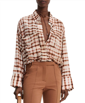 A person wearing the Dorothee Schumacher Checked Statement Blouse, characterized by its oversized style with wide sleeves in a brown and white plaid pattern, tucked partly into high-waisted brown pants.