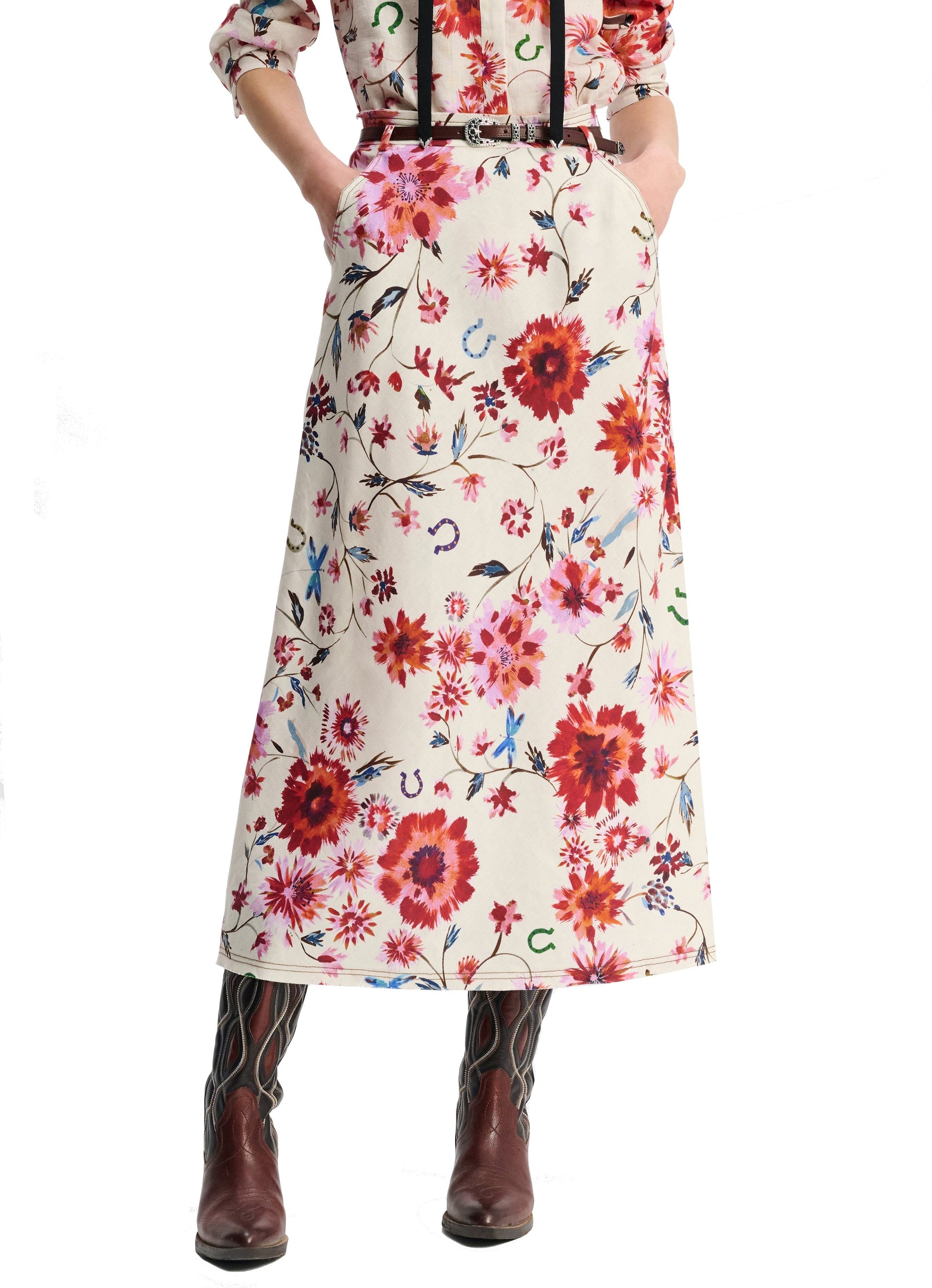 A person wearing the Dorothee Schumacher Floral Ease Skirt along with a matching blouse, accented by a leather tie belt and cowboy boots, stands casually with hands tucked into pockets.