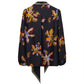 The Dorothee Schumacher Floral Seductive Blouse by Dorothee Schumacher is a black silk blouse adorned with a vibrant flower print, featuring long sleeves and an asymmetric collar, and finished with a pointed tie at the back.