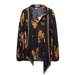 The Dorothee Schumacher Floral Seductive Blouse by Dorothee Schumacher is a long-sleeved black silk blouse adorned with a colorful flower print, featuring a V-neckline and an asymmetric hem.