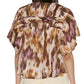 Rear view of a person wearing the Isabel Marant Leaza Top, a loose-fit, short-sleeved cotton voile blouse in brown, purple, and cream print with a pleated yoke, paired with light-colored pants.