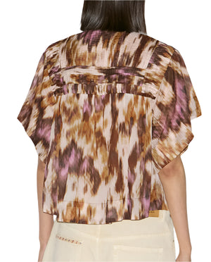 Rear view of a person wearing the Isabel Marant Leaza Top, a loose-fit, short-sleeved cotton voile blouse in brown, purple, and cream print with a pleated yoke, paired with light-colored pants.