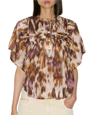 A person wearing the Isabel Marant Leaza Top, a loose-fit blouse crafted from printed cotton voile, featuring short sleeves, ruffled details, and a buttoned front.